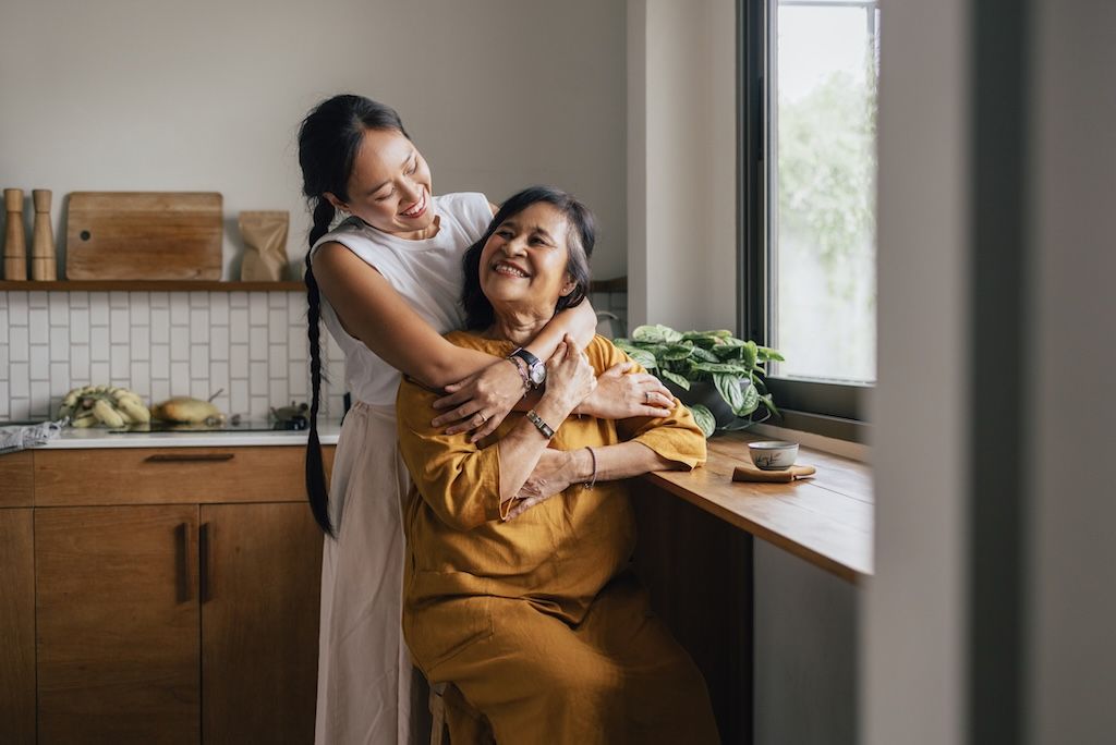 woman-hugging-older-adult-parent-in-kitchen