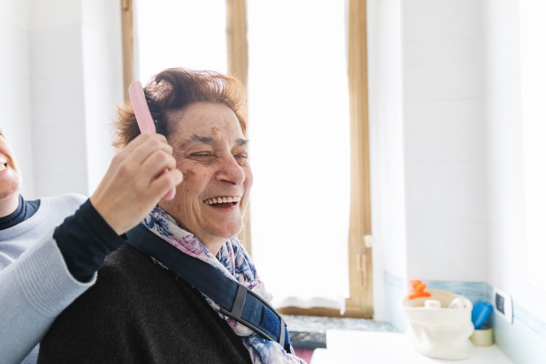 Older woman getting her hair brushed by a caregiver