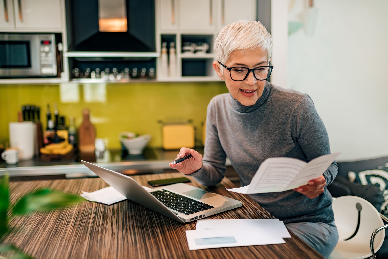 older-adult-woman-looking-at-documents-and-her-computer