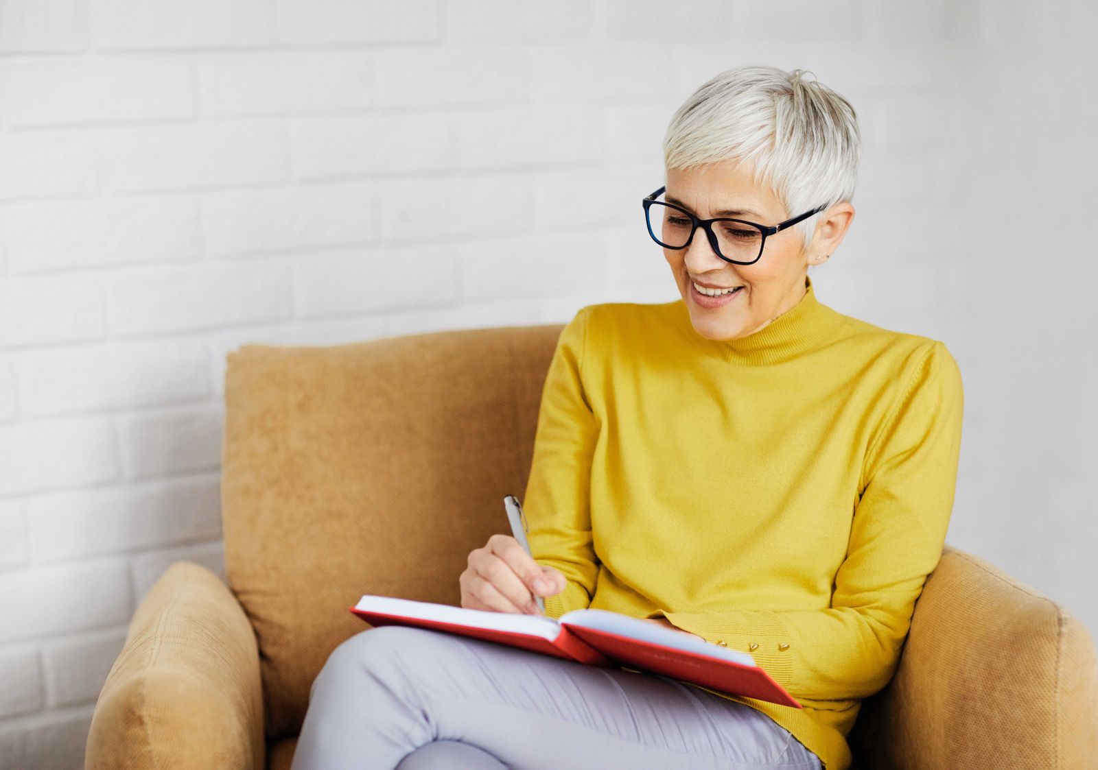 older woman in a yellow shirt and glasses sitting in a chair while writing