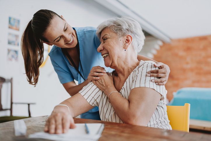 older woman at table embracing standing caretaker