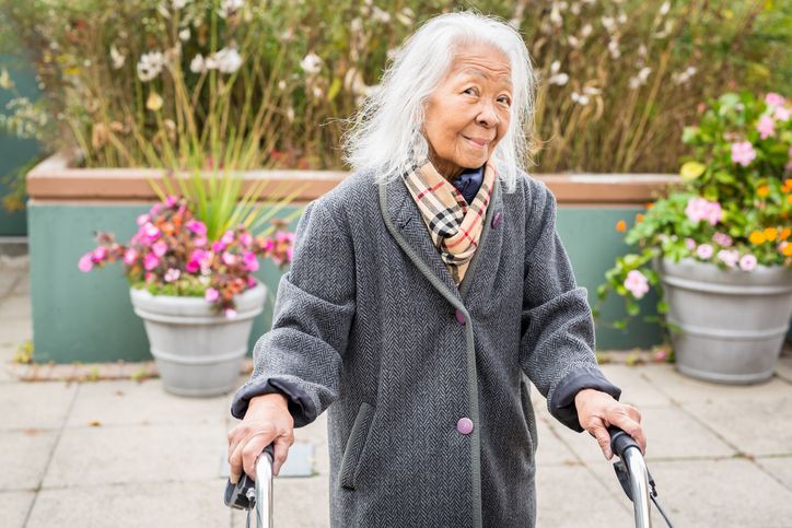 older woman smiling while using a walker outside