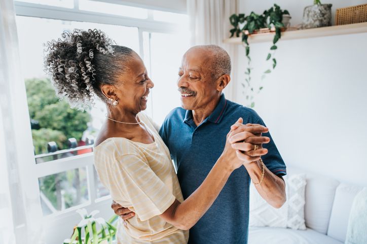 older couple dancing in room in front of a window