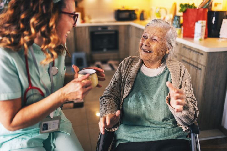 caregiver handing an older woman in a wheelchair a cup of coffee