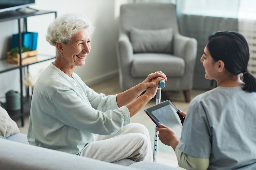 older woman and caregiver sitting and talking with tablet
